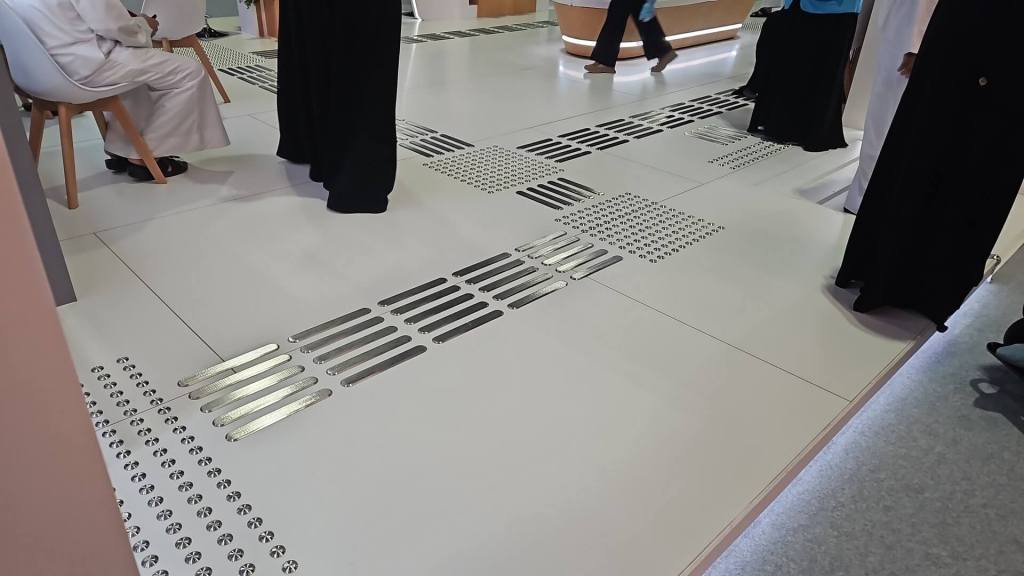 A modern floor design featuring metallic strips and dotted patterns, with people walking nearby and one person seated in a traditional outfit.