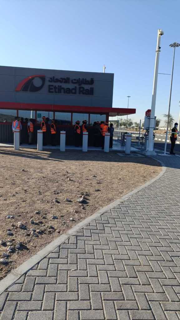Exterior view of the Etihad Rail station with people in safety vests gathered at the entrance.