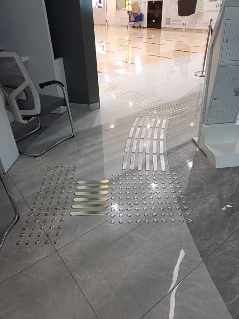 Installation of stainless steel tactile studs and directional lines on a tiled floor in Al Barsha Government Service Center, enhancing accessibility.