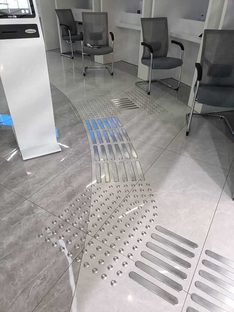 Tactile installation featuring stainless steel studs and directional lines on tiled flooring in a government service center, enhancing accessibility.