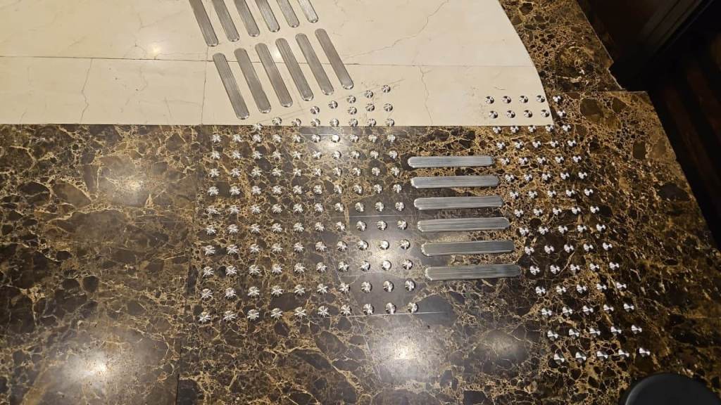 A floor covered with stainless steel tactile studs and directional strips arranged for installation on a marble surface.