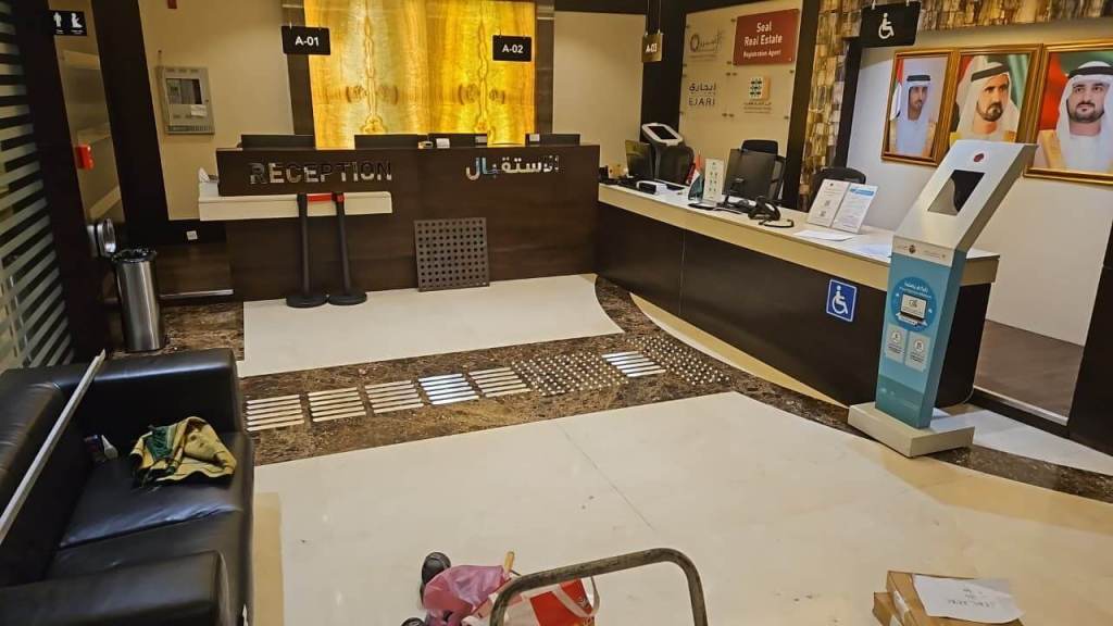 Interior view of a reception area in a real estate office in Dubai, featuring a black sofa, a reception desk with computer equipment, and tactile installation on the floor for accessibility.