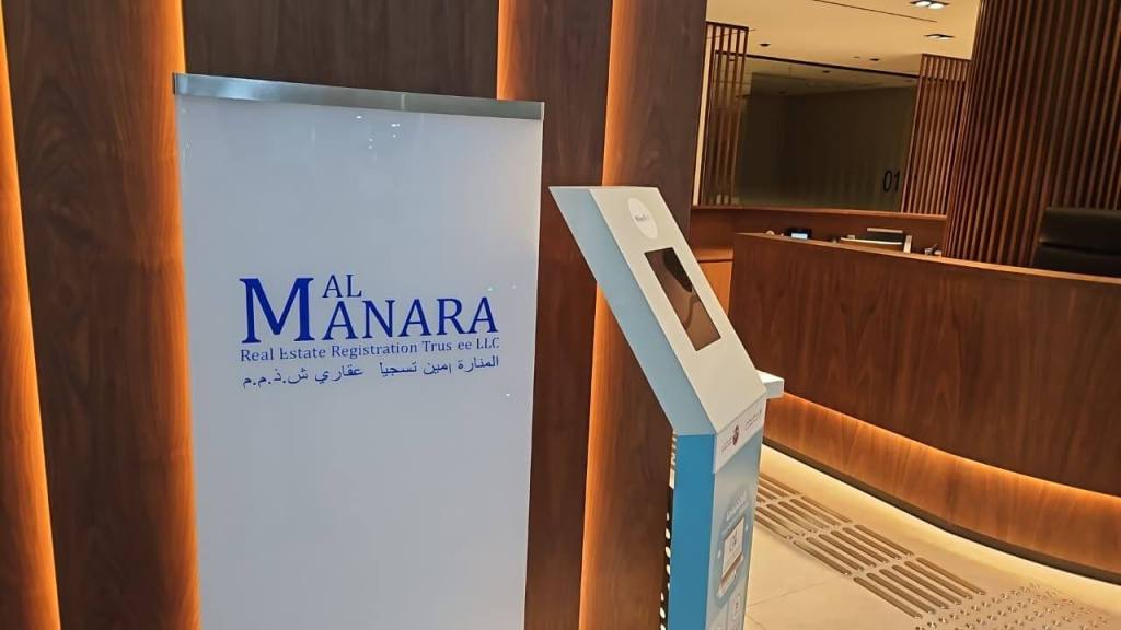 Interior view of the Al Manara Real Estate Registration Trustee LLC office, featuring a sign with the organization's name and details, alongside a digital kiosk for visitor assistance.