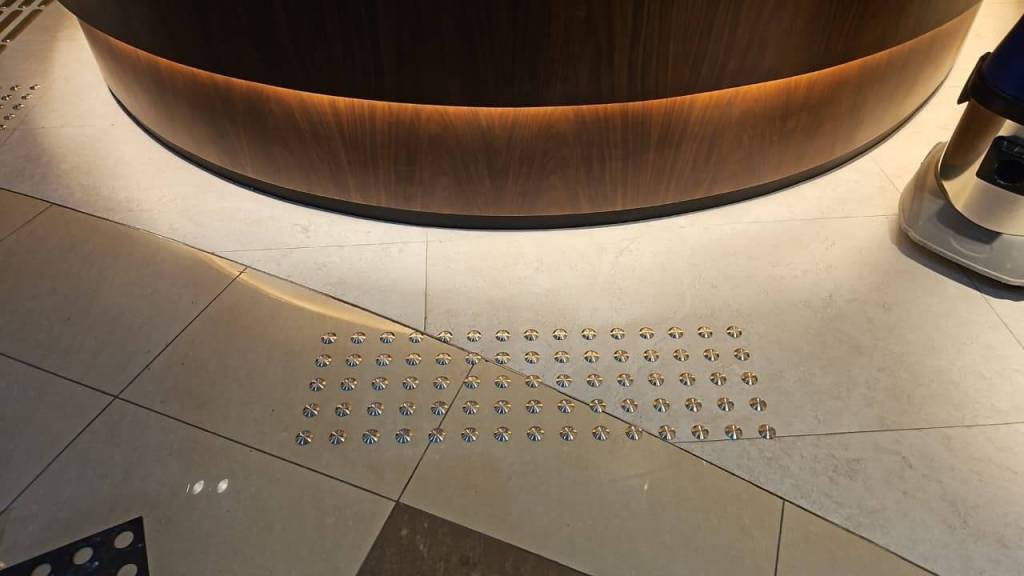 Close-up view of stainless steel tactile studs installed on a smooth floor surface near a rounded reception desk in the Real Estate Registration Trustee LLC office.
