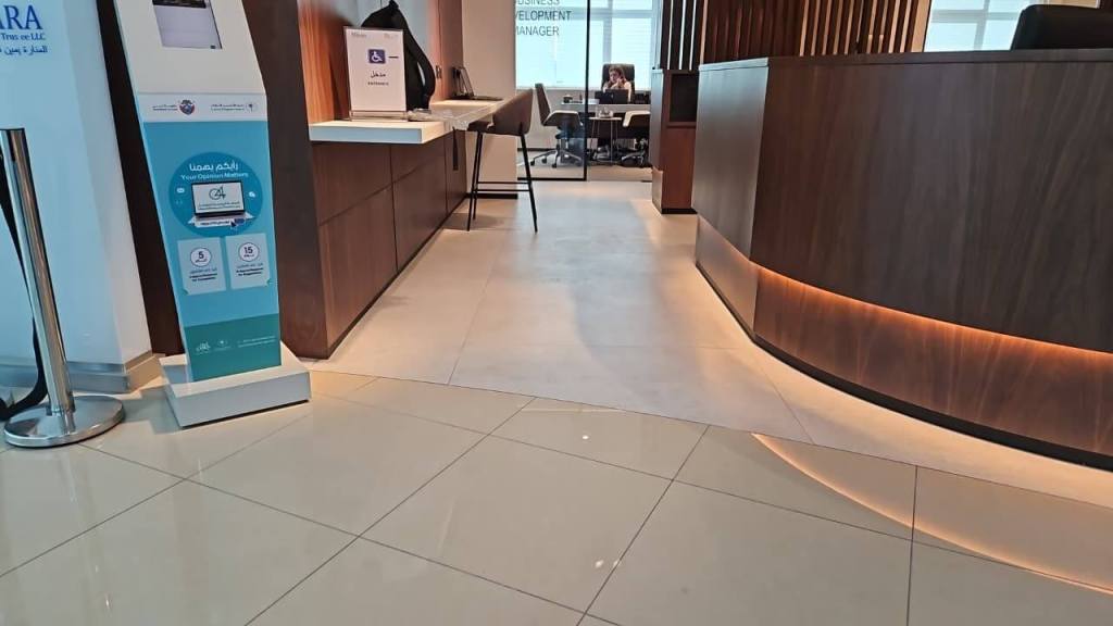 Interior view of the Real Estate Registration Trustee LLC office in Al Manara Centre, Dubai, showcasing a reception area with wooden accents, a service desk, and a digital kiosk.