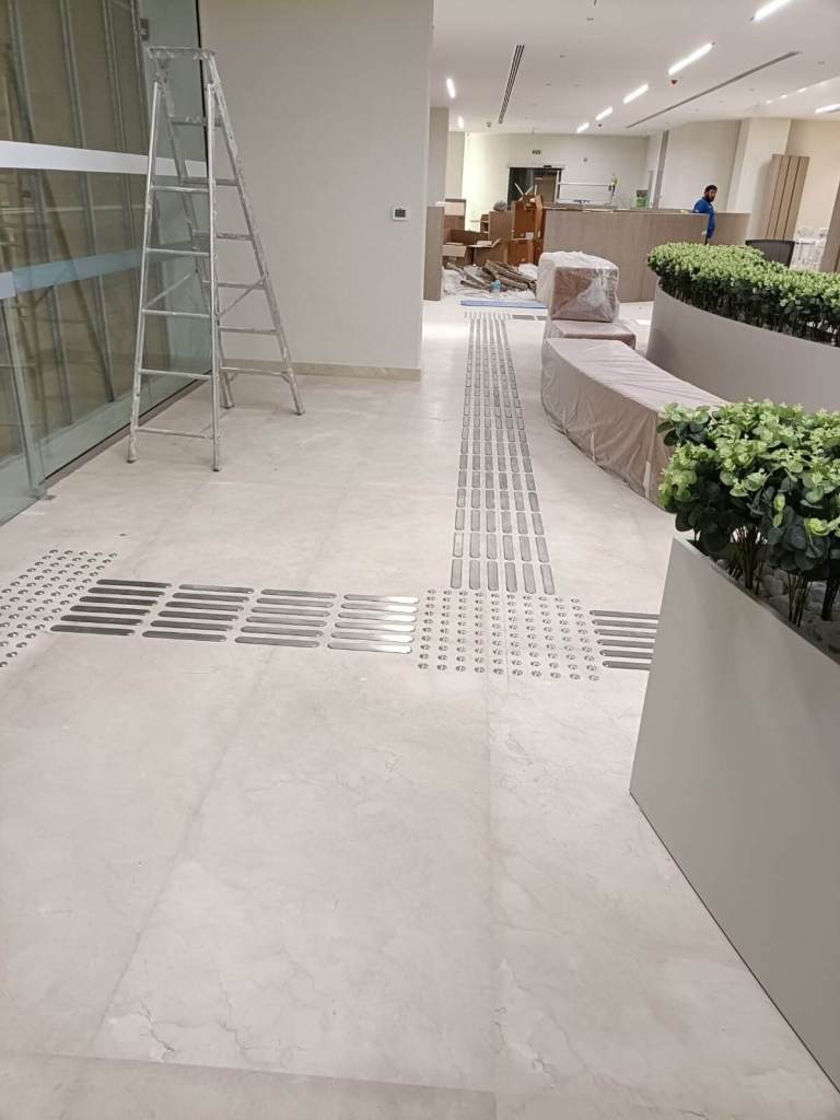 Interior view of the Dubai Court at Manara Mall, showcasing tactile stainless steel strips and studs installed on the floor for accessibility.