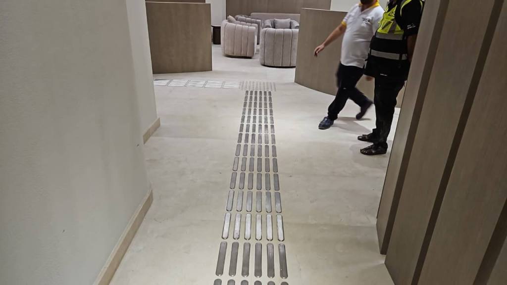 Two individuals walking near tactile stainless steel strips installed on the floor of the Dubai Court at Manara Mall, enhancing accessibility for visually impaired visitors.