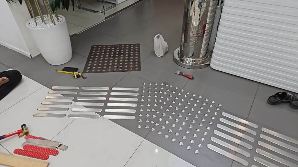 Installation site for stainless steel tactile self-adhesive studs and lines at On Time Business Solution in Dubai, with tools such as hammers and a measuring tape visible.