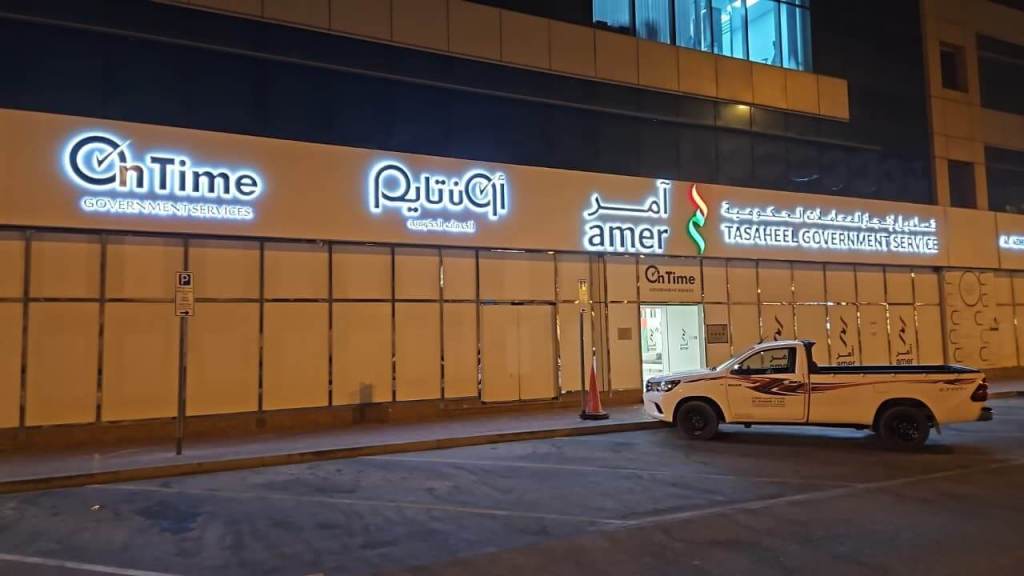 Exterior view of 'On Time Government Services' office building in Dubai at night, featuring illuminated signage and a parked pickup truck.