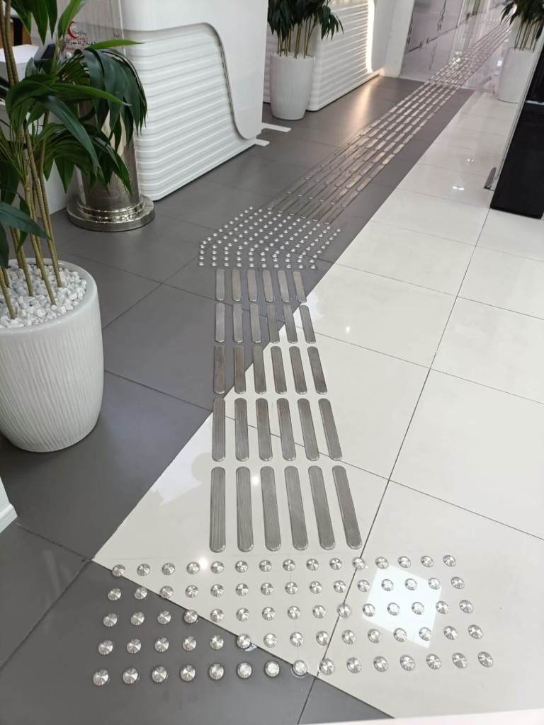 View of stainless steel tactile self-adhesive studs and lines installed on the floor, enhancing accessibility in an office environment.