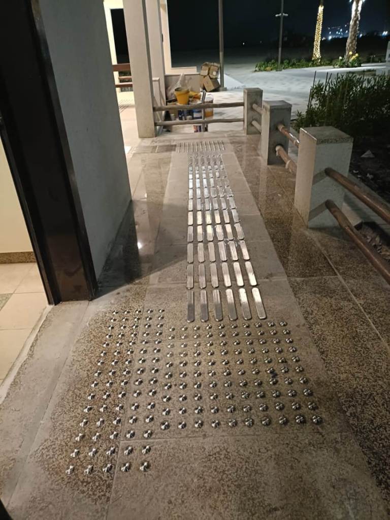Installation of stainless steel tactile pin-type studs and lines on a pathway at Majlis Al Bahar, Jumeirah, enhancing accessibility for visually impaired individuals.