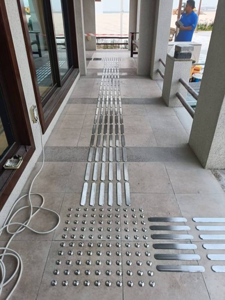 Installation of stainless steel tactile pin-type studs and lines on a tiled walkway for improved accessibility at Prime FM, Majlis Al Bahar, Jumeirah.