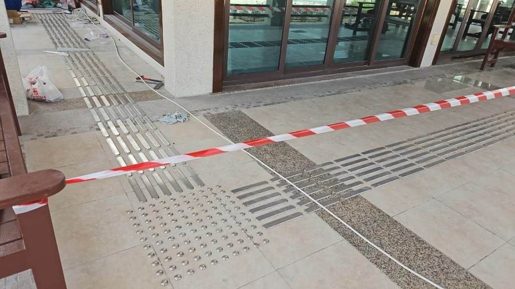 Installation of stainless steel tactile pin-type studs and lines in a walkway area at Majlis Al Bahar, Jumeirah. The image shows the alignment of tactile indicators and safety tape marking the working area.