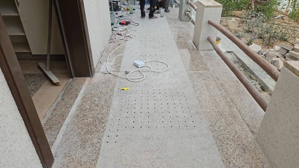 Installation area showing stainless steel tactile pin-type studs set in the ground, with visible tools and equipment nearby.