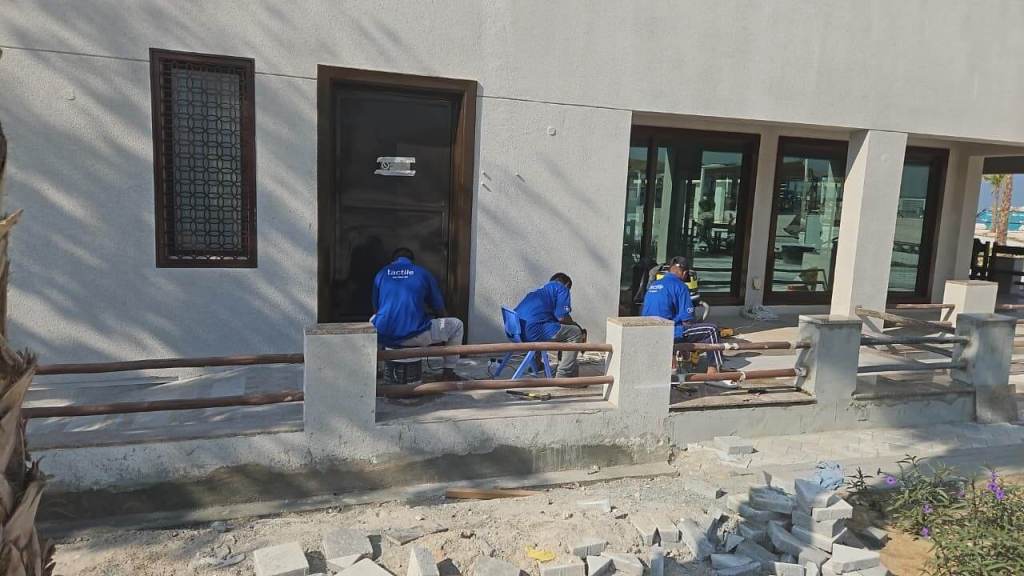 Workers installing tactile indicators outside Majlis Al Bahar, Jumeirah, with tools and materials visible.