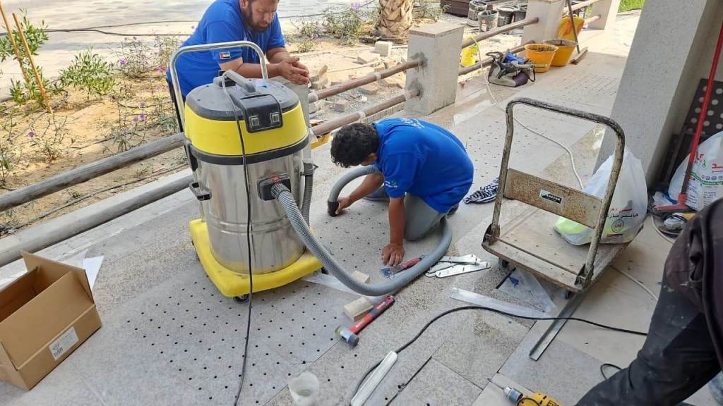 Workers using a vacuum cleaner to prepare the flooring for the installation of tactile indicators at Majlis Al Bahar, Jumeirah.