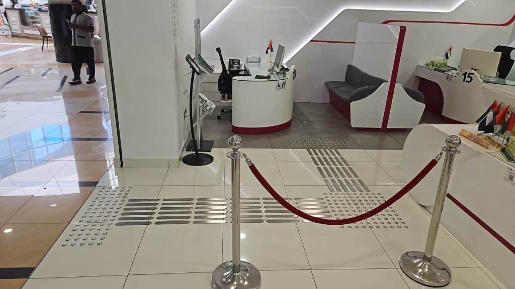 Interior view of a service desk area with seating, polished floor tiles, and barrier ropes in place. Multiple flags are displayed.