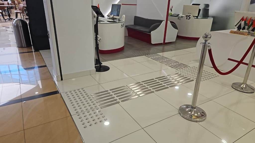 Interior view of a modern reception area featuring tiled floors, a queue barrier, and tactile guiding strips on the floor.