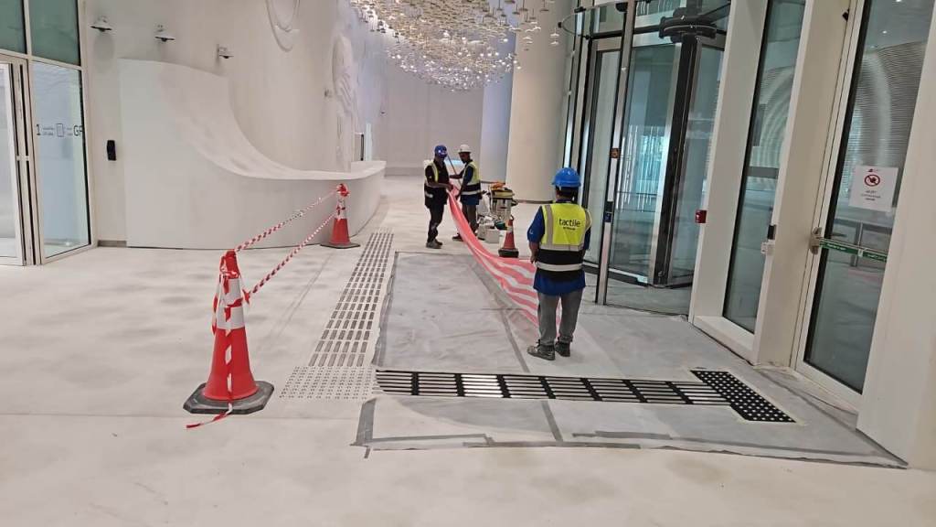 Construction workers in safety vests and helmets manage a work area with traffic cones and caution tape inside a modern building under renovation.