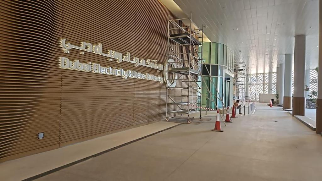 Interior view of Dubai Electricity and Water Authority building under construction, featuring a wooden wall with the name displayed in Arabic and English, scaffolding, and construction cones.