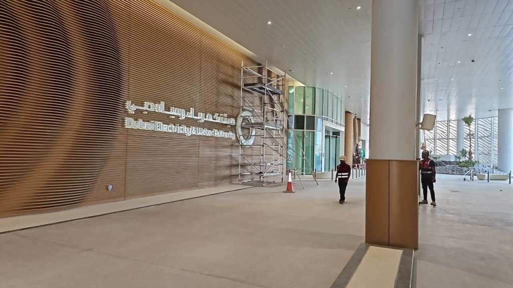 Exterior view of the Dubai Electricity and Water Authority building under construction, featuring wooden paneling and work scaffolding with two workers visible.
