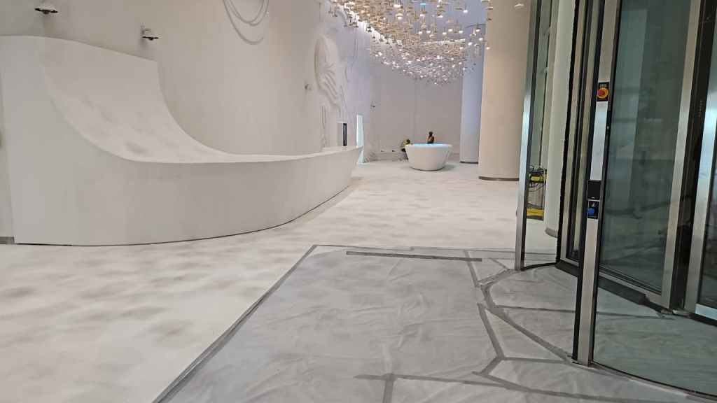 Interior view of a modern, minimalist space with a curved white reception desk, a smooth white floor, and artistic lighting fixtures hanging from the ceiling.