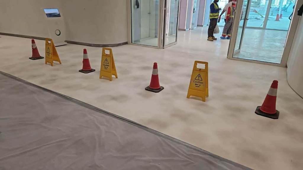 A hallway with wet floor caution signs and traffic cones, with construction workers in the background.