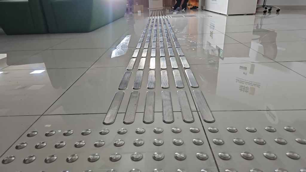 A close-up view of tactile paving on a tiled floor, featuring textured strips and domes for aiding navigation.