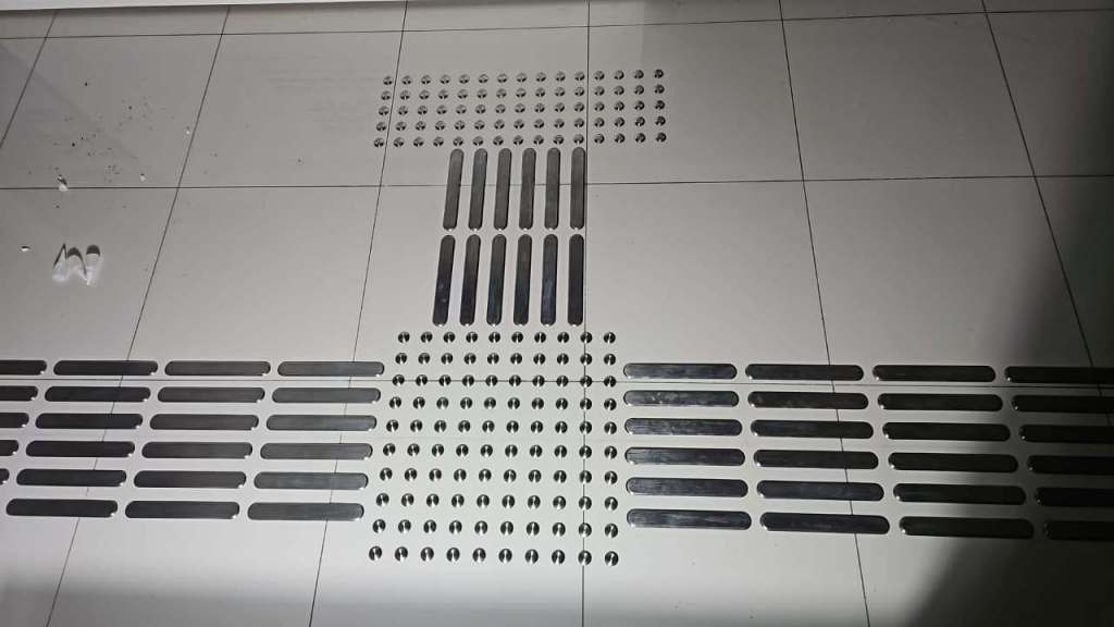 A close-up view of a tiled floor featuring various textured metal strips, including long, short, and circular designs, arranged in a pattern.