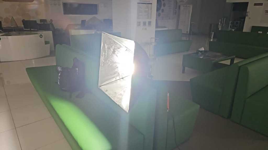 A brightly lit softbox light positioned near a green sofa in a modern indoor space with minimal furniture.