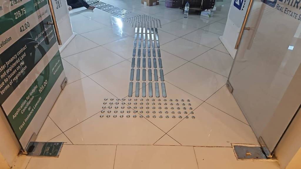 Interior hallway featuring a tiled floor with metallic tactile indicators for navigation, alongside informational signage.