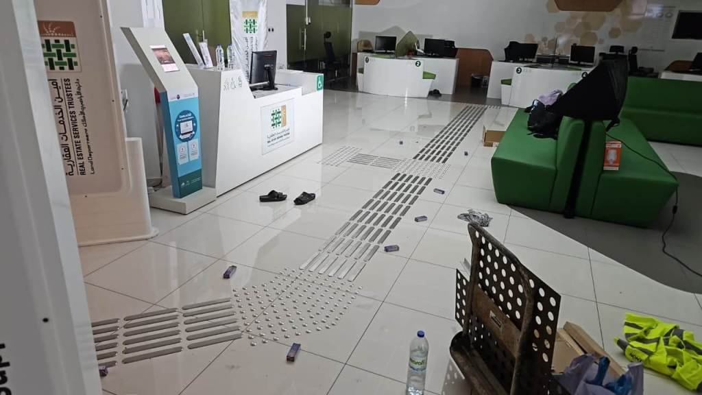 An interior view of an office space showing a tiled floor with scattered personal items, a water bottle, and renovation materials, alongside modern furniture and computer stations.