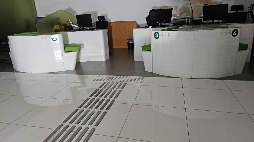 Modern reception area with two white desks featuring green chairs and computer monitors, set on a tiled floor with a drainage system.