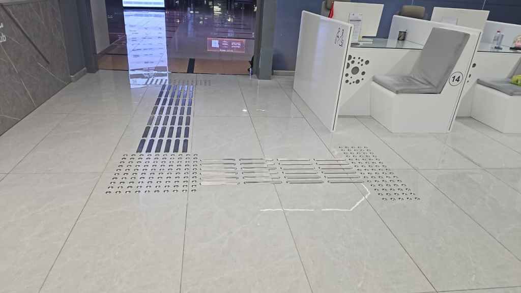 A view of a modern tiled floor featuring various patterns of drainage grates and textured areas, with seating areas visible in the background.