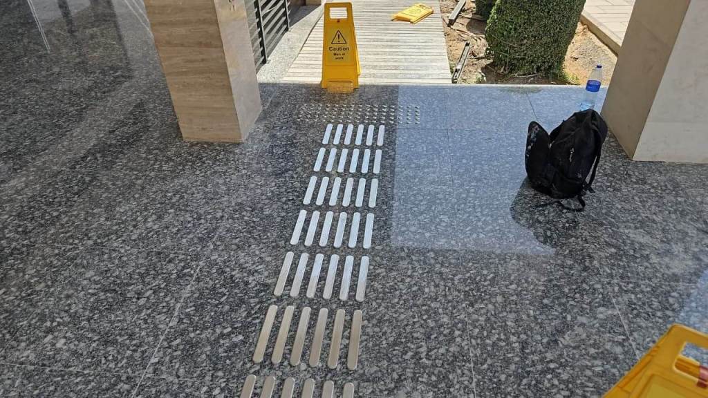A shiny granite floor with safety markers and a caution sign indicating a wet area, alongside a backpack and a water bottle.