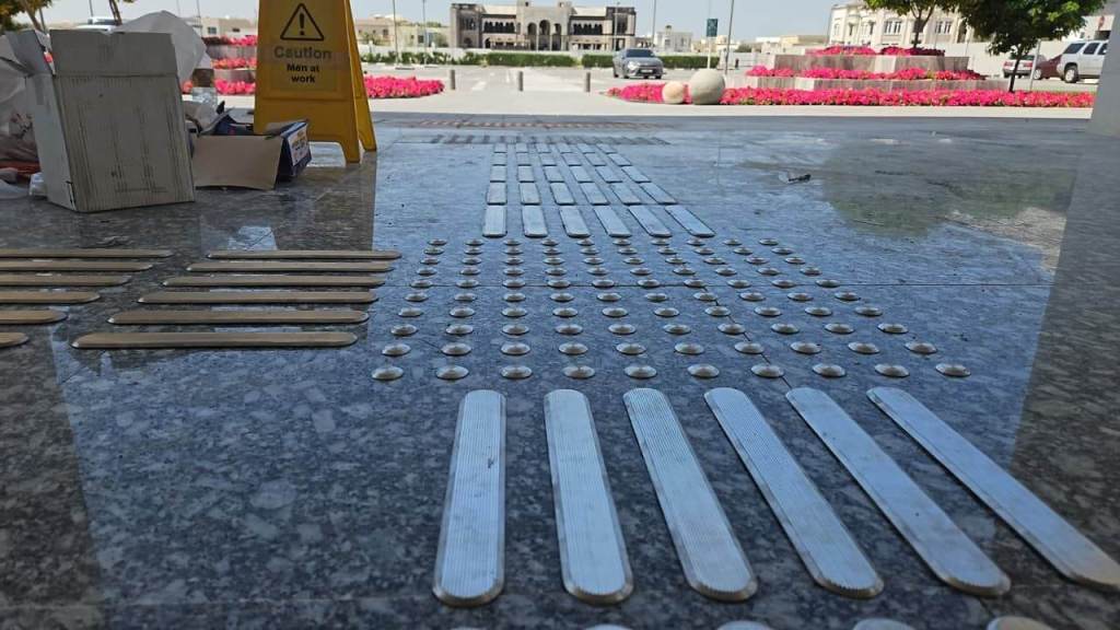 Close-up view of tactile paving strips on a marble floor, with a caution sign indicating construction work nearby.