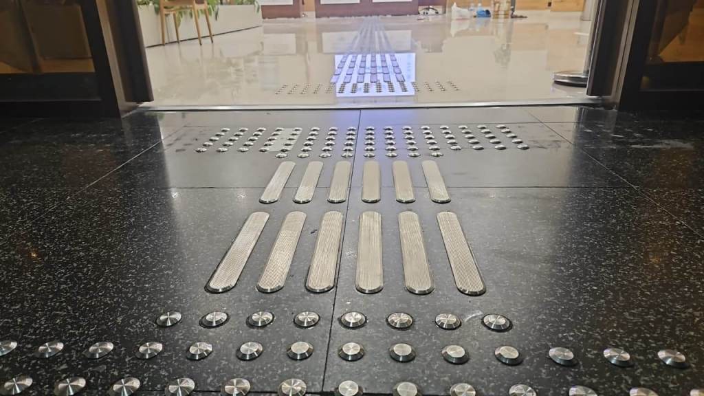 Close-up view of a textured floor featuring tactile paving and guidance strips in an entrance area.