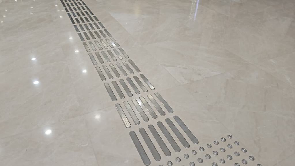 A close-up view of a marble floor featuring a metallic tactile path with evenly spaced inserts, designed for navigation.
