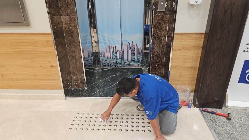 A technician kneeling on the floor, installing floor tiles near an elevator, with a cityscape backdrop.