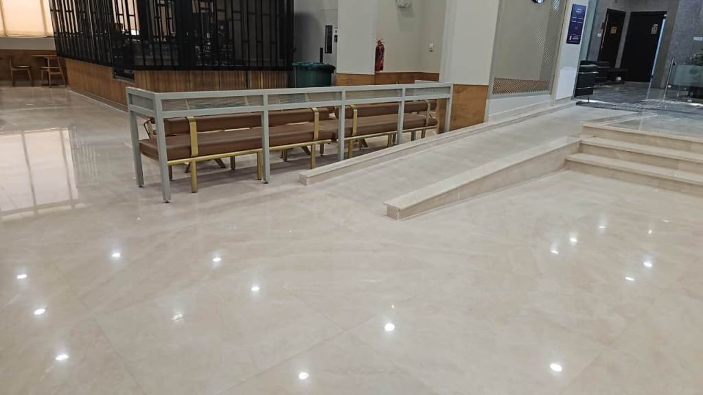 A modern indoor area featuring polished marble flooring, bench seating in a waiting area, and a gentle ramp leading to a set of steps.