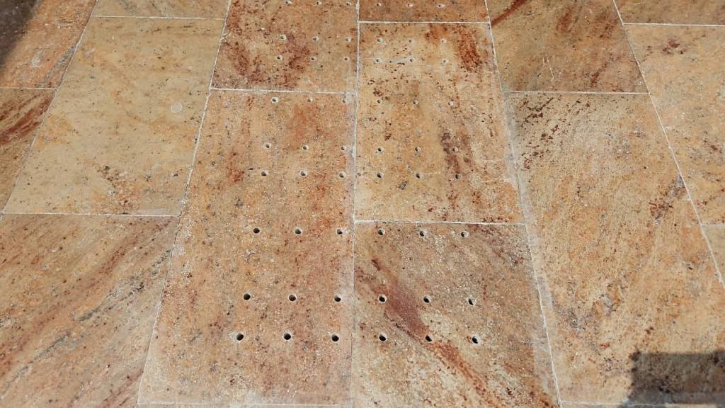 Close-up of a textured stone floor featuring various shades of brown with drilled holes in a grid pattern.