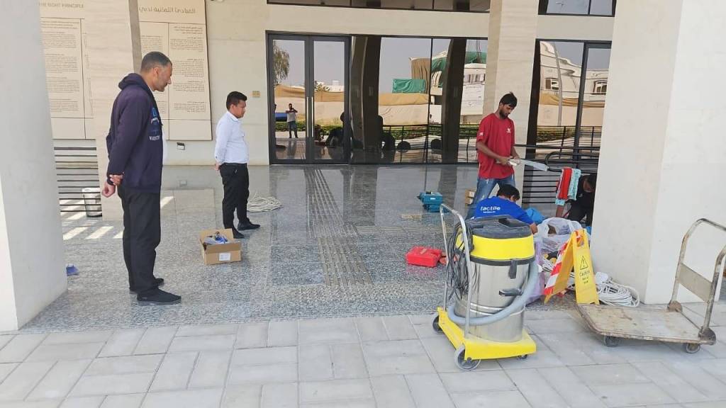 Two men observing work being done in an outdoor area, where other workers are organizing equipment and cleaning supplies.
