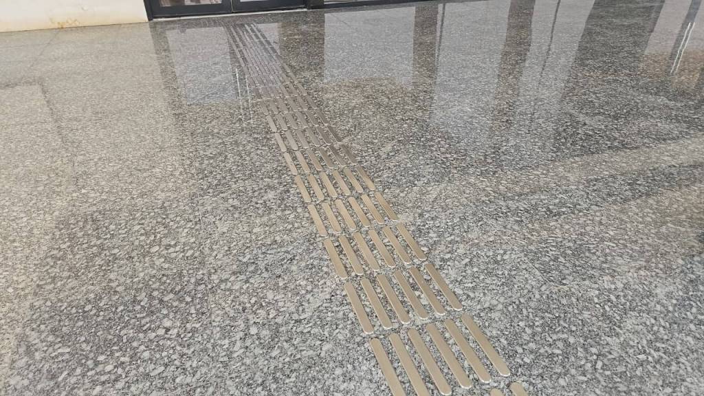 Close-up view of a smooth granite floor featuring a tactile guiding strip composed of metal elements.