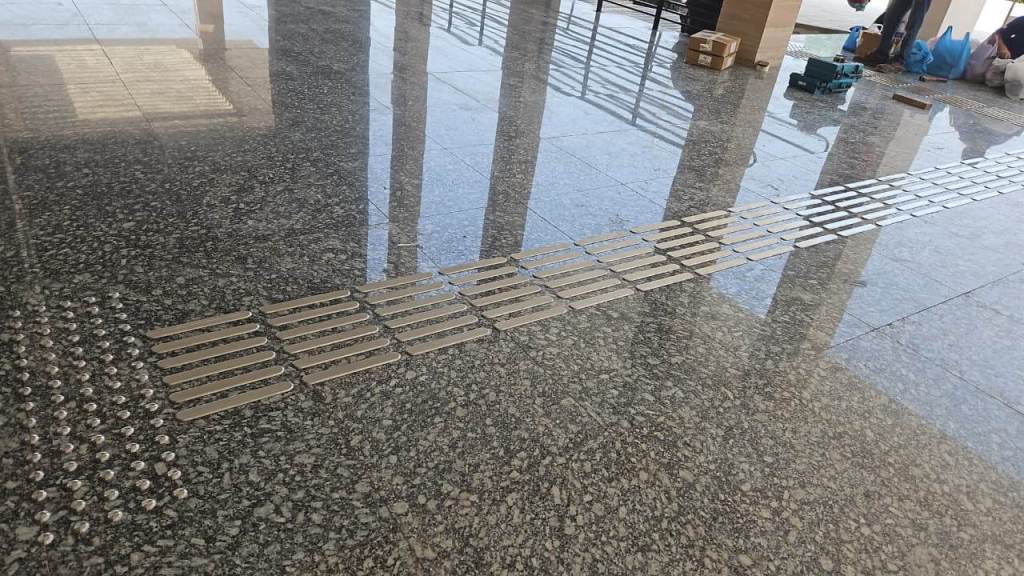 A smooth granite floor featuring a row of metal tactile guide strips used for navigation, with construction equipment and boxes visible in the background.