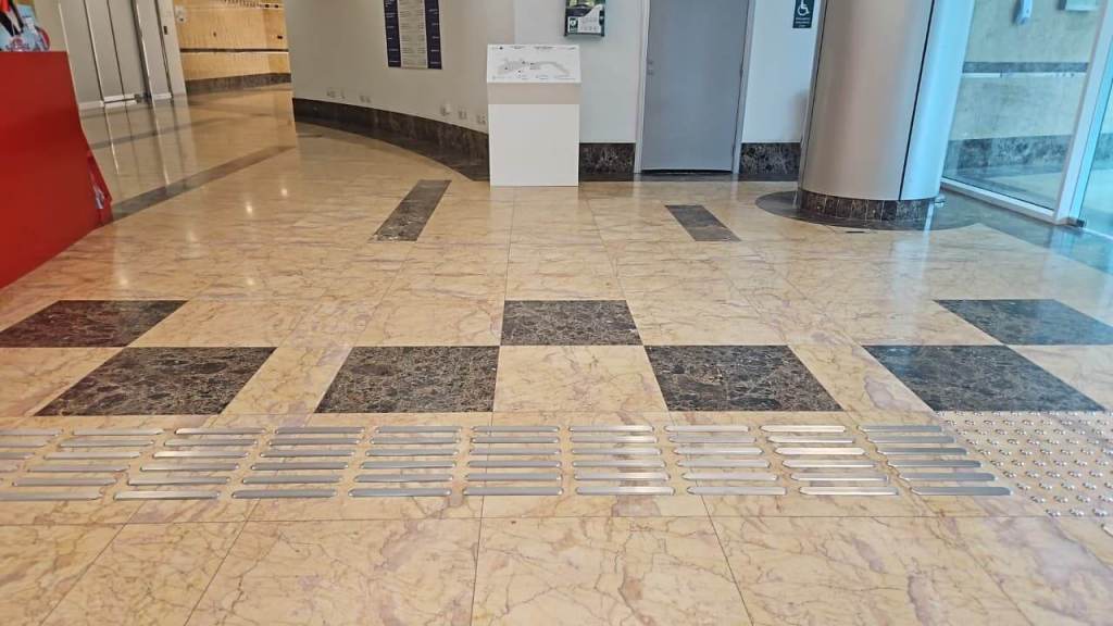 Interior view of a lobby with patterned marble flooring, featuring tactile guidance strips along the ground.