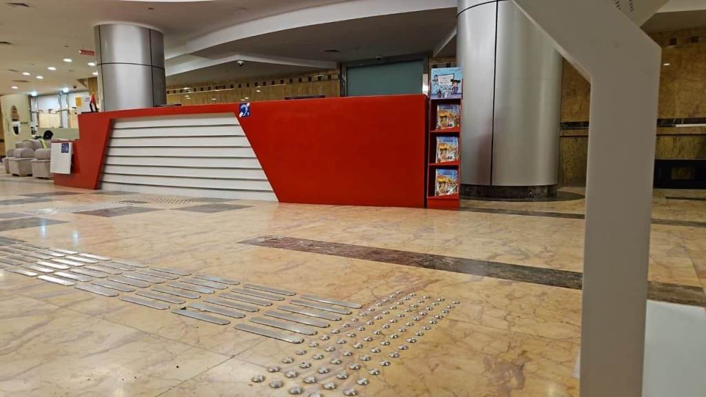 Interior view of a reception area featuring a modern red reception desk with white panels, surrounded by marble flooring and seating areas.