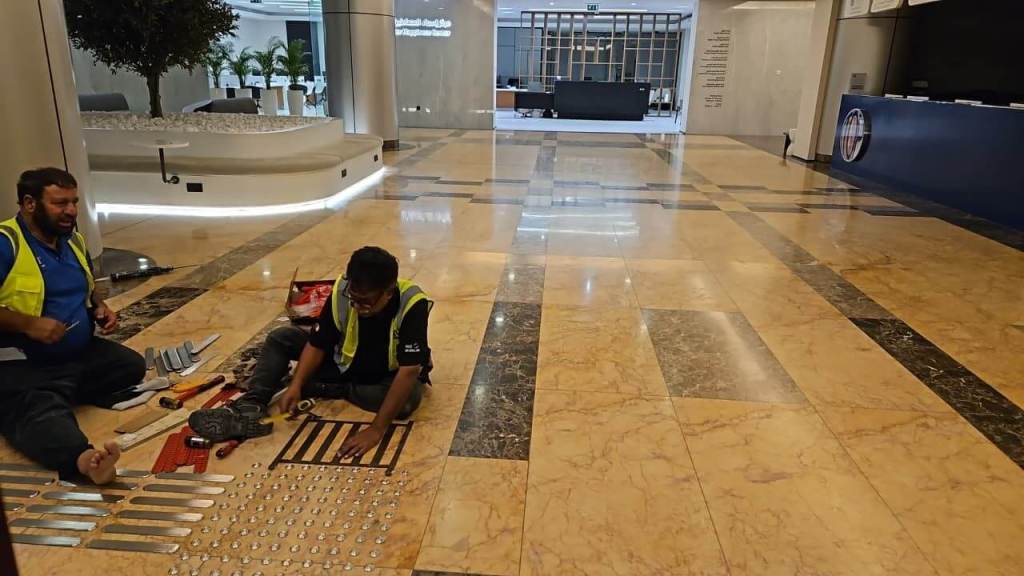 Two workers in safety vests performing maintenance on the floor of a modern lobby, surrounded by tools and equipment.