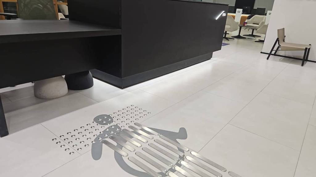 A modern interior featuring a sleek black reception area and a distinctive floor graphic resembling a person. The flooring incorporates tactile elements and patterns, contributing to an accessible design.