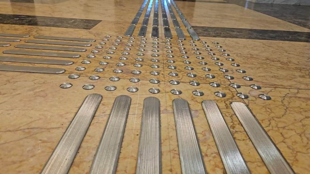 Close-up view of a floor surface featuring metal strips and textured dots for tactile guidance in an indoor space.