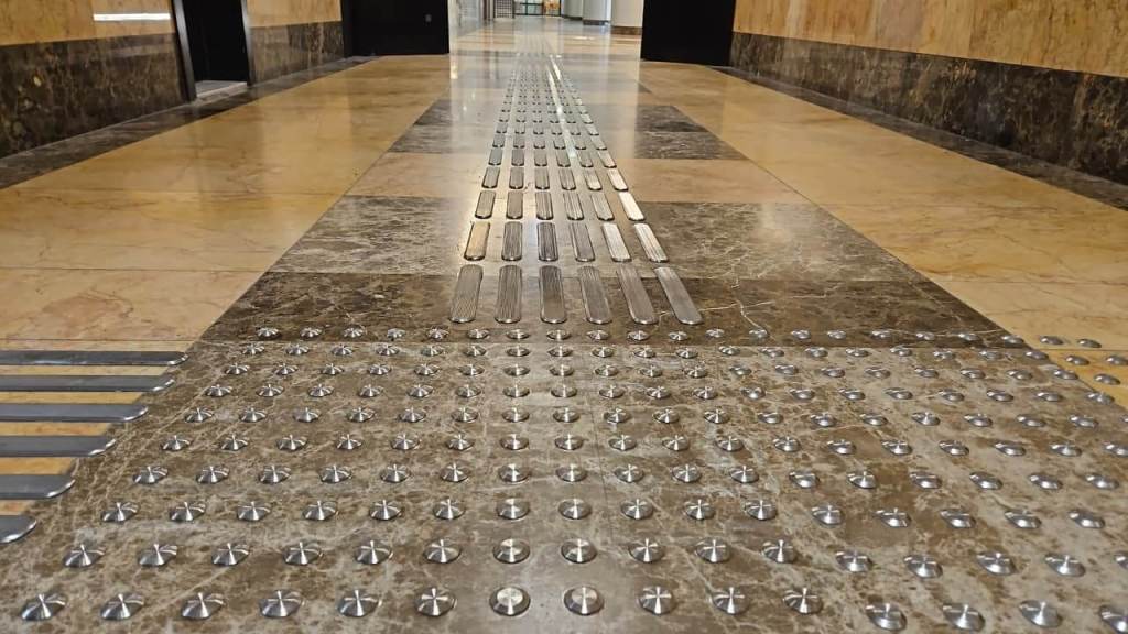 Close-up view of a smooth marble floor featuring tactile ground surface indicators with multiple raised patterns for improved navigation.